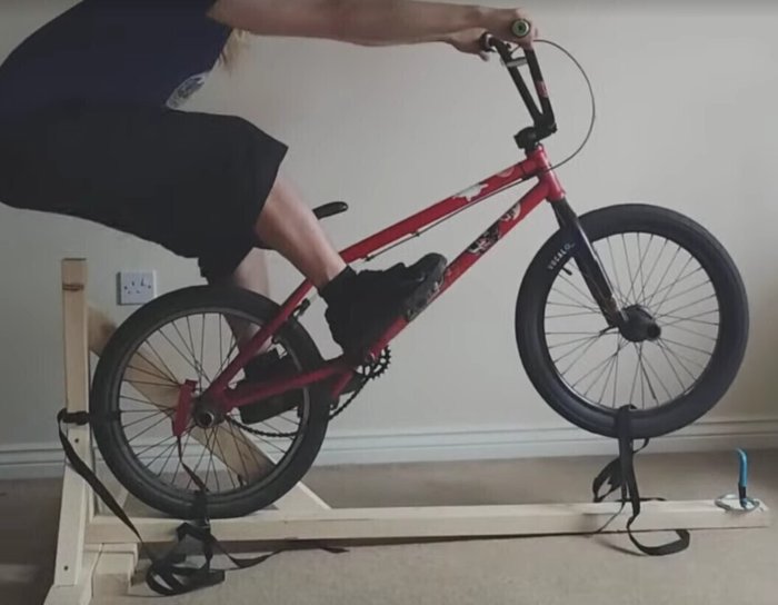 Photo of someone using a bmx to practice manuals on a wooden frame for support